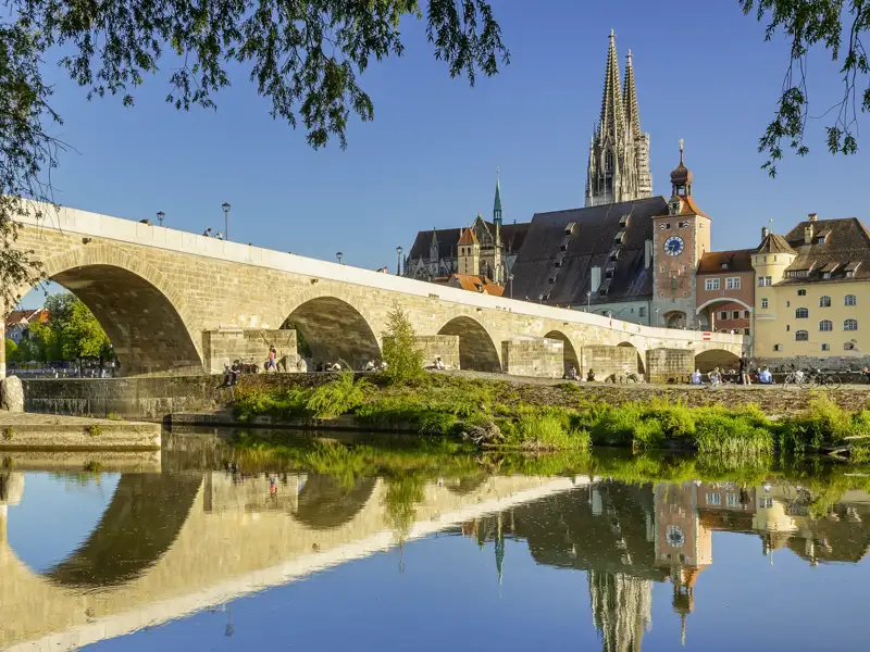 Die Steinerne Brücke in Regensburg mit dem Dom St. Peter im Hintergrund, gespiegelt im ruhigen Wasser der Donau, ein Highlight unserer Studiosus Rundreise.