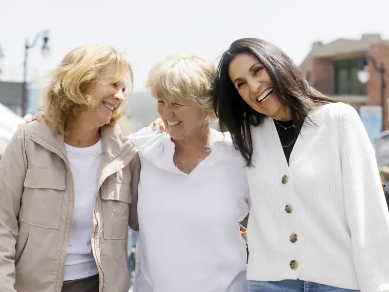 Drei gut gelaunte Frauen spazieren während einer geführten Gruppenreise mit Studiosus lachend und Arm in Arm durch eine Stadt.