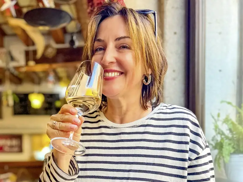 Lächelnde Frau in einem Restaurant, die während ihrer Studienreise ein Glas Weißwein und lokale Spezialitäten genießt.