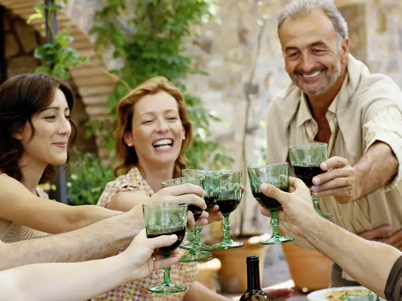 Fröhliche Reisegruppe auf einer Studienreise stößt bei einer Weinprobe im Piemont mit Rotwein an.