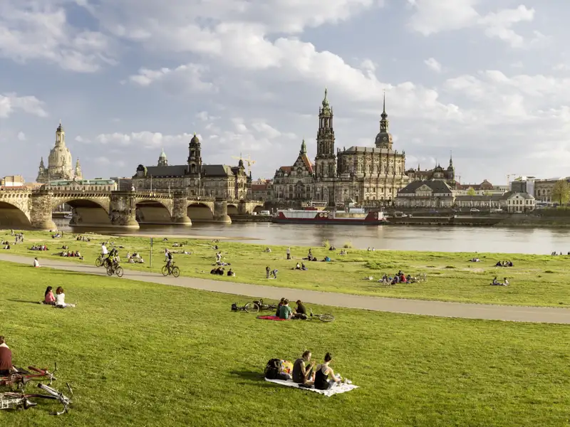 Der berühmte Canaletto-Blick auf Dresdens Altstadt mit Augustusbrücke über die Elbe, davor Menschen auf den sonnigen Elbwiesen, ein Ausblick, den wir auch auf unserer Gruppenreise mit Studiosus genießen.