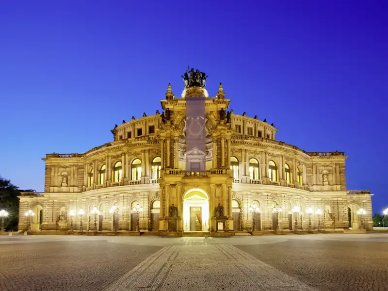 Prachtvolle Fassade der Semperoper in Dresden, bei Dämmerung golden beleuchtet vor einem tiefblauen Abendhimmel, ein Ausblick, welchen wir auch auf unserer Rundreise mit Studiosus genießen werden.