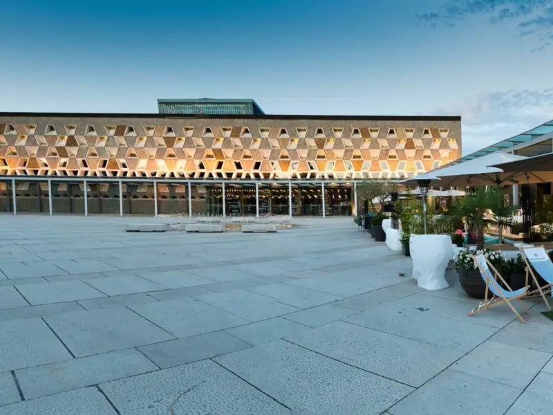 Moderne Architektur des Grand Théatre in Luxemburg bei Dämmerung mit beleuchteter Wabenfassade und Vorplatz mit Terrasse, ein Highlight jeder Studiosus Eventreise