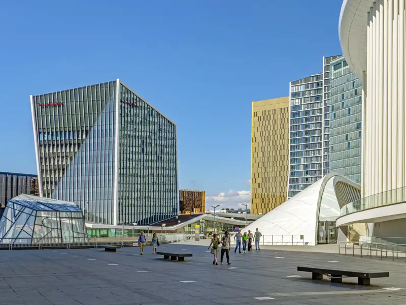 Eine kleine Gruppe spaziert auf dem sonnigen Platz vor der Philharmonie im modernen Kirchberg-Quartier in Luxemburg, ein Ausflug, den wir auch auf unserer Studosus Gruppenreise machen werden.