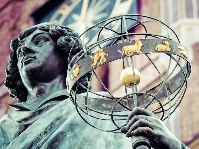 Nahaufnahme des Kopernikus-Denkmals in Torun, das eine Armillarsphäre mit goldenen Tierkreiszeichen hält, ein Highlight unserer Gruppenreise mit Studiosus nach Polen.