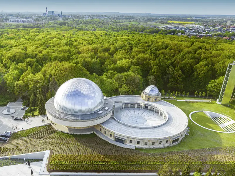Vogelperspektive auf das Schlesische Planetarium bei Kattowitz mit seiner silbernen Kuppel inmitten einer dichten Waldlandschaft, ein Highlight unserer Rundreise mit Studiosus nach Polen.