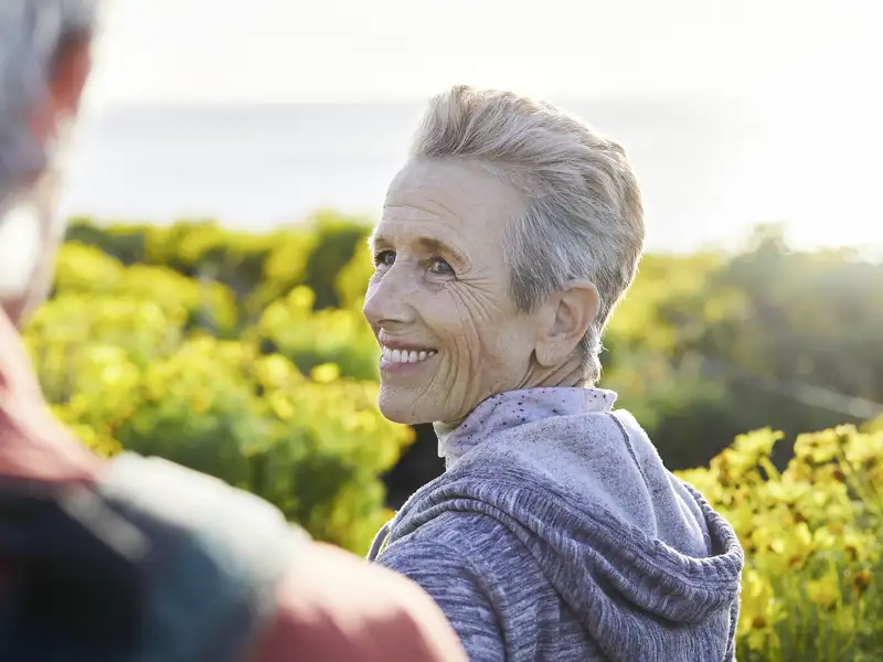 Lächelnde Frau genießt mit ihrem Partner die Aussicht über ein gelbes Blütenmeer während einer Wanderung auf Elba, ein toller Ausflug auf unserer Gruppenreise mit Studiosus.