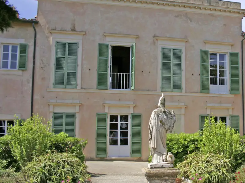 Außenansicht von Napoleons Villa dei Mulini in Portoferraio auf Elba mit einer Statue im Vordergrund und grünen Fensterläden, ein Highlight unserer Rundreise durch Italien.