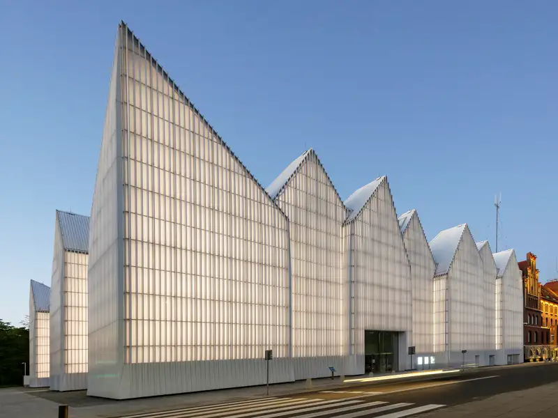 Die moderne Fassade der Stettiner Philharmonie leuchtet bei Dämmerung, ein architektonisches Highlight der Studienreise mit Studiosus nach Polen.
