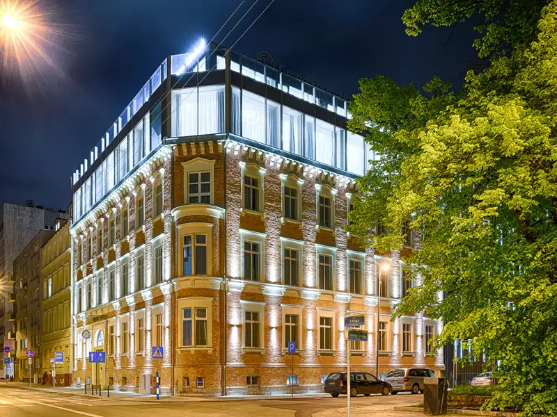 Die historische Backsteinfassade des Hotels Radisson Blu in Stettin leuchtet in der Nacht unter einem modernen Glasaufbau.