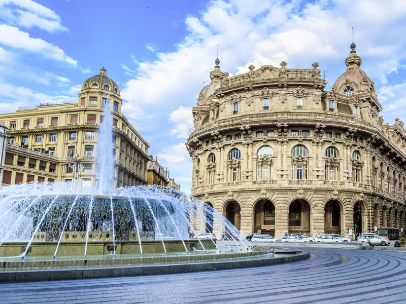 Der imposante Springbrunnen auf der Piazza De Ferrari in Genua vor prachtvollen Palazzi unter einem leicht bewölkten Himmel, welchen wir auf unserer Gruppenreise mit Studiosus bewundern.