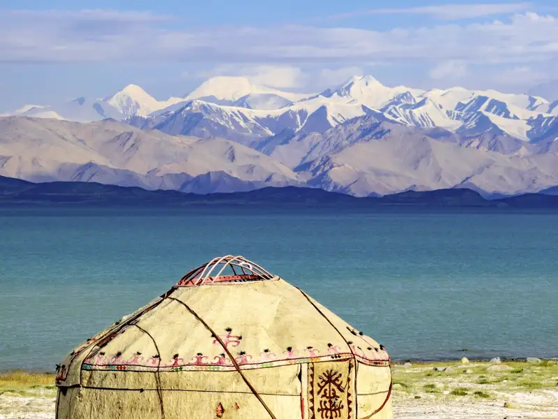 Traditionelle Jurte am Ufer des tiefblauen Issyk-Kul-Sees vor dem schneebedeckten Panorama des Tianshan-Gebirges, ein toller Ausblick auf unserer Gruppenreise mit Studiosus.