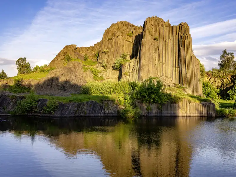 Auf unserer Gruppenreise mit Studiosus sehen wir, wie sich die imposanten Basaltsäulen des Herrenhausfelsens (Panská skála)  im ruhigen Wasser eines Sees in Tschechien spiegeln.