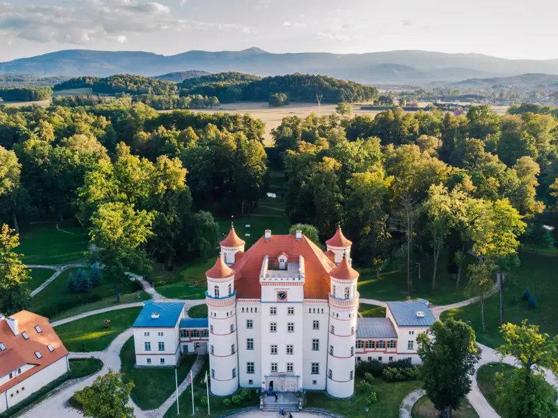 Prachtvolles Schloss Wojanów mit roten Türmen, umgeben von einem Park im Hirschberger Tal vor der Kulisse des Riesengebirges, ein toller Anblick auf unserer Gruppenreise mit Studiosus.