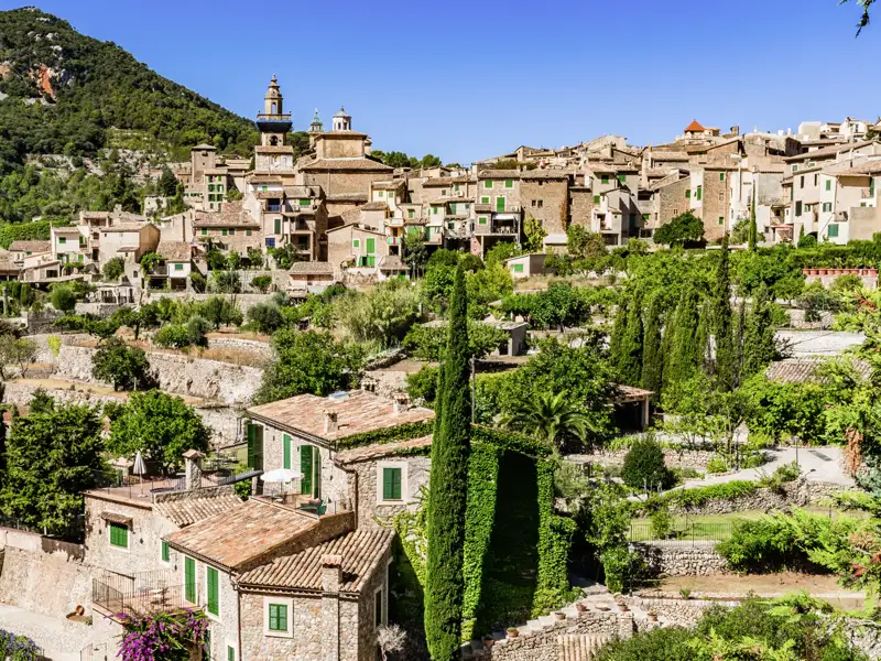 Auf einer Gruppenreise mit Studiosus genießen wir den Blick auf die Steinhäuser und Terrassengärten des Bergdorfs Valldemossa auf Mallorca an einem sonnigen Tag.