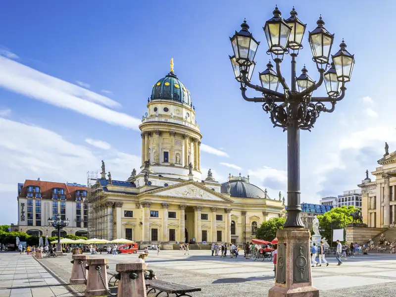 Der Deutsche Dom auf dem belebten Gendarmenmarkt in Berlin bei Sonnenschein, mit einer verzierten Laterne im Vordergrund, ein toller Anblick auf unserer Gruppenreise mit Studiosus nach Berlin.