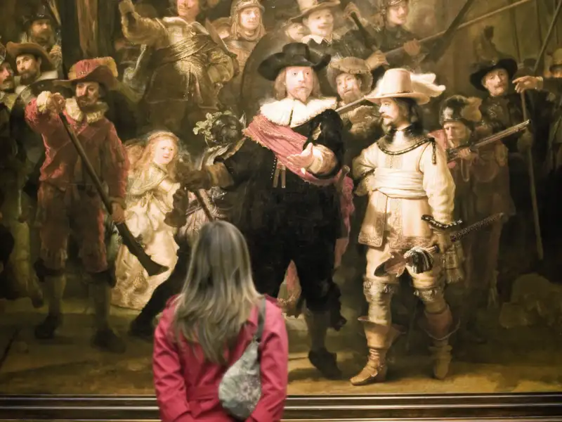 Teilnehmerin einer Studiosus Studienreise betrachtet Rembrandts berühmtes Gemälde 'Die Nachtwache' im Rijksmuseum Amsterdam.