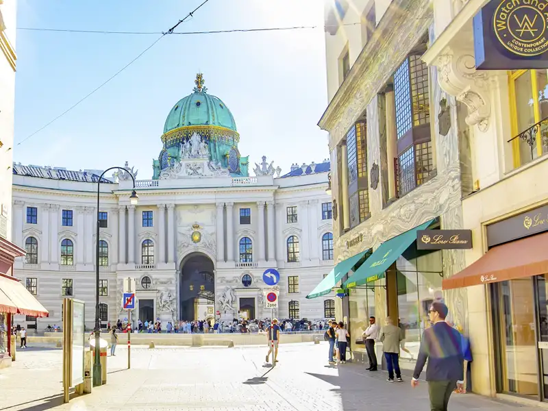 Sonniger Blick durch eine Wiener Einkaufsstraße auf den prachtvollen Michaelertrakt der Hofburg mit seiner markanten Kuppel, den Sie auf einem Bummel mit Ihrer Studiosus Reisegruppe  genießen können