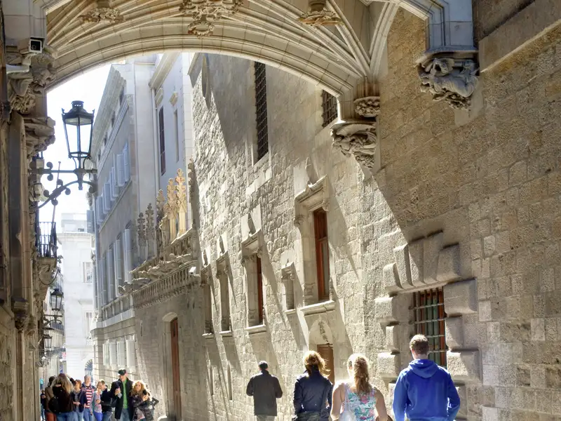Eine Studiosus-Gruppenreise erkundet das sonnige Gotische Viertel in Barcelona und passiert die Brücke Pont del Bisbe.