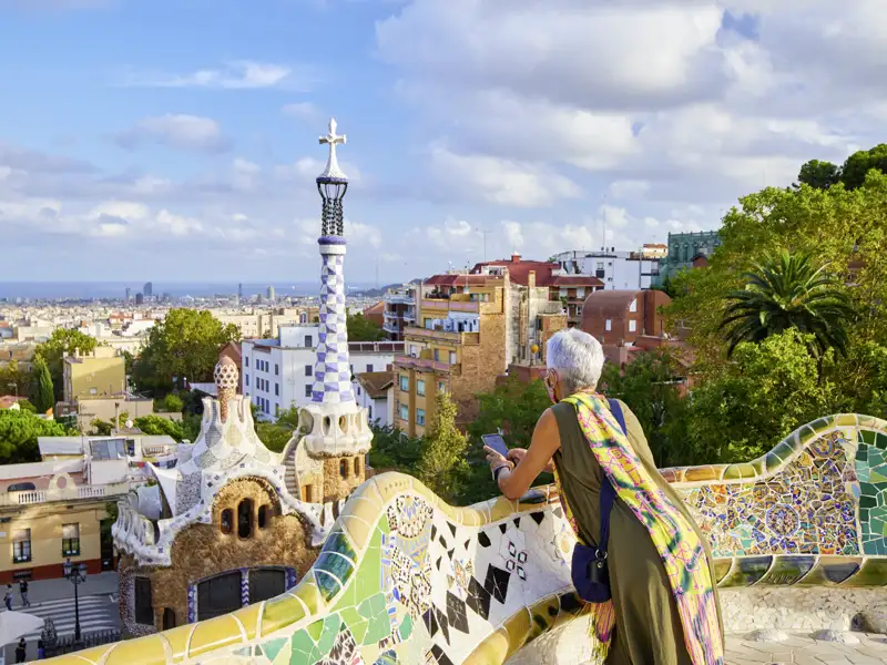 Auf unserer Gruppenreise mit Studiosus genießt eine Reisende auf der berühmten Mosaikbank im Parc Güell den weiten Blick über die Dächer von Barcelona.
