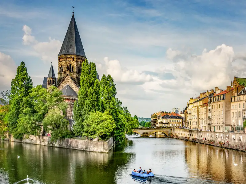 Der historische Temple Neuf in Metz auf einer kleinen Insel der Mosel, davor ein Ausflugsboot und die Altstadtfassaden, ein Highlight auf unserer Gruppeneise mit Studiosus.