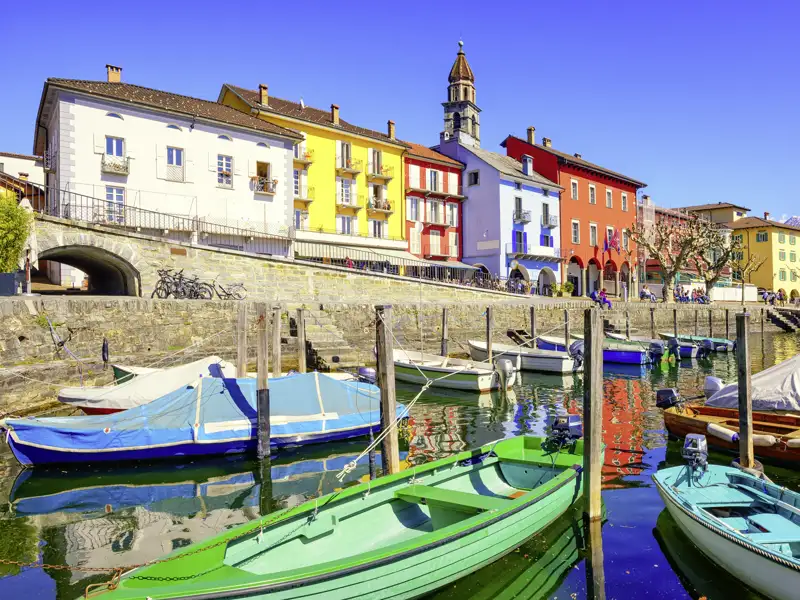 Farbenfrohe Häuserzeile am ehemaligen Fischerhafen von Ascona mit kleinen Booten auf dem Lago Maggiore, ein Highlight unserer Gruppenreise mit Studiosus.