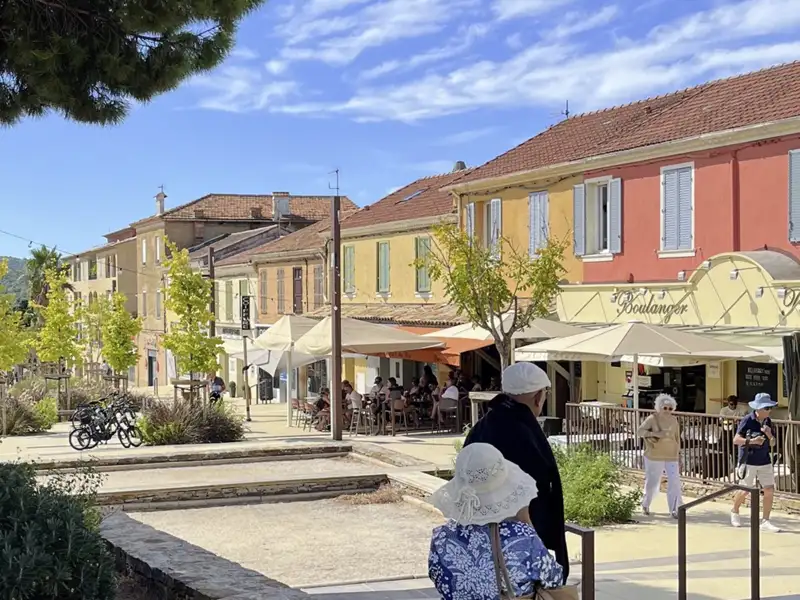 Teilnehmer einer Studienreise flanieren durch die Gassen von Bormes-les-Mimosas vorbei an bunten Häusern und Cafés.