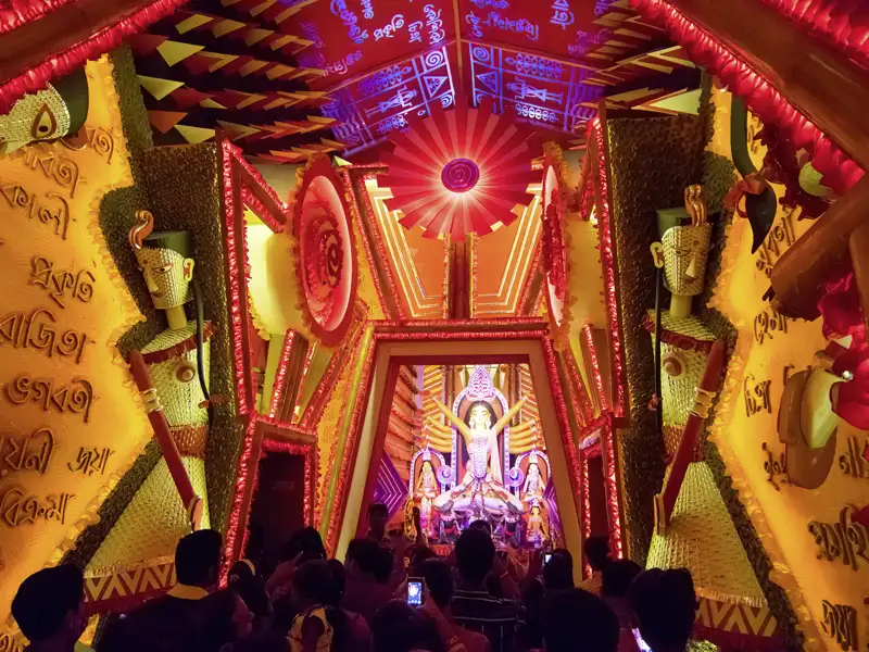 Während unserer Eventreise mit Studiosus sehen wir Gläubige und Reisende vor einem prächtigen, rot-goldenen Pandal mit der Statue der Göttin Durga während der Durga Puja in Kolkata.