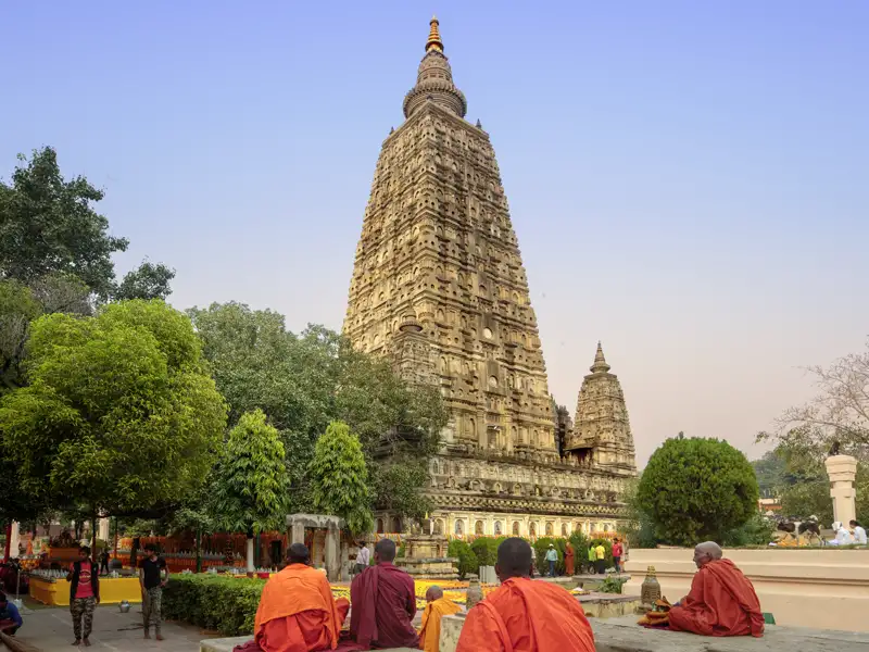 Auf unserer Eventreise mit Studiosus erleben wir, wie Buddhistische Mönche in orangen Roben andächtig vor dem imposanten Mahabodhi-Tempel sitzen, UNESCO-Welterbe in Bodhgaya.