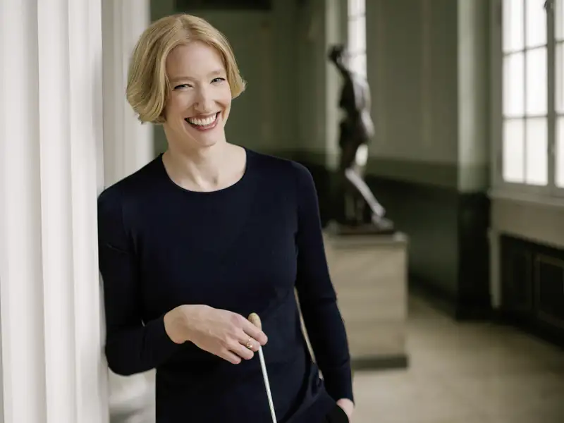 Die Dirigentin Joana Mallwitz lehnt lächelnd mit Taktstock an einer Säule. Sie ist ein Star-Gast beim Musikfestival Kissinger Sommer.