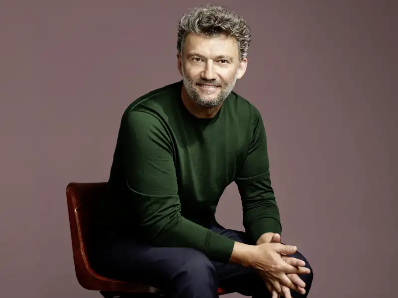 Der Star-Tenor Jonas Kaufmann sitzt lächelnd auf einem Stuhl, zu erleben bei dieser Studiosus Eventreise in Neapel.