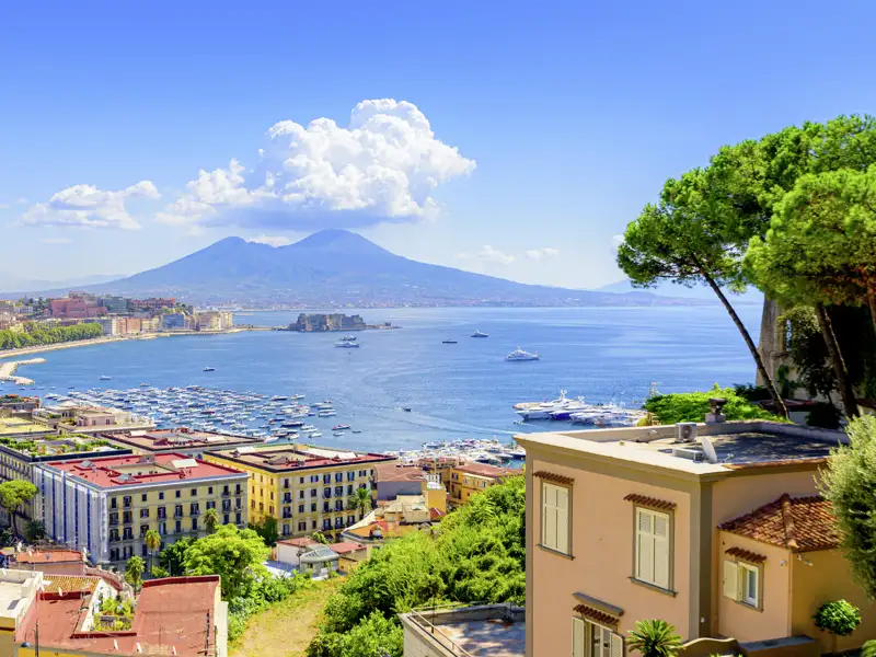 Sonnige Aussicht über den Golf von Neapel mit Jachthafen, bunten Häusern und dem majestätischen Vulkan Vesuv am Horizont, ein Highlight unserer Gruppenreise mit Studiosus.