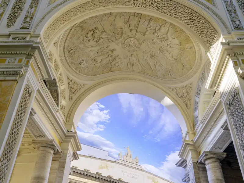 Blick durch eine prachtvolle Arkade mit aufwendiger Stuckdecke auf die Fassade des Teatro San Carlo in Neapel, ein toller Anblick auf unserer Gruppenreise mit Studiosus.
