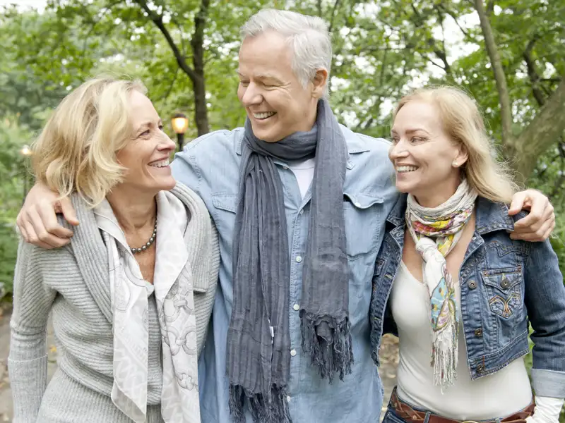 Drei gut gelaunte Teilnehmer einer Gruppenreise mit Studiosus spazieren Arm in Arm durch den Central Park in New York und lachen miteinander.