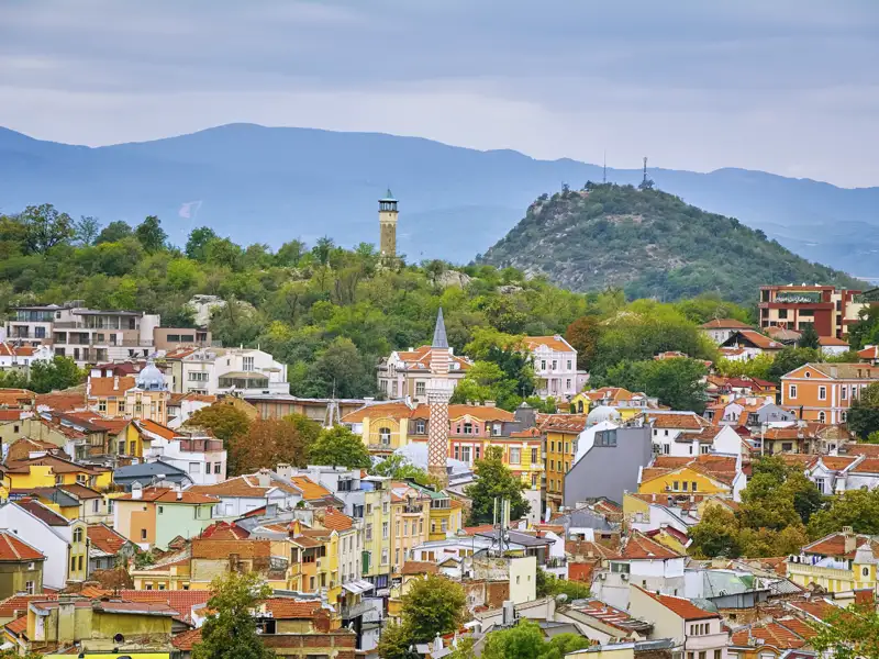 Blick über die Altstadt von Plovdiv während eines Stadtrundgangs, mit traditionellen Häusern,dem Minarett der Dschumaja-Moschee und einem der charakteristischen grünen Hügel der Stadt im Hintergrund.