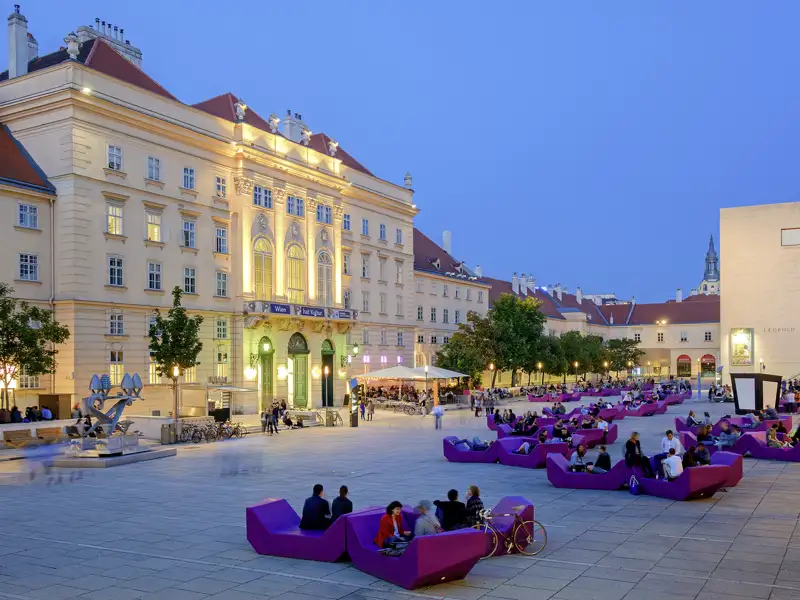 Auf unserer Gruppenreise mit Studiosus genießen wir die Abenddämmerung im MuseumsQuartier Wien auf den ikonischen lila Sitzmöbeln vor den Museen.