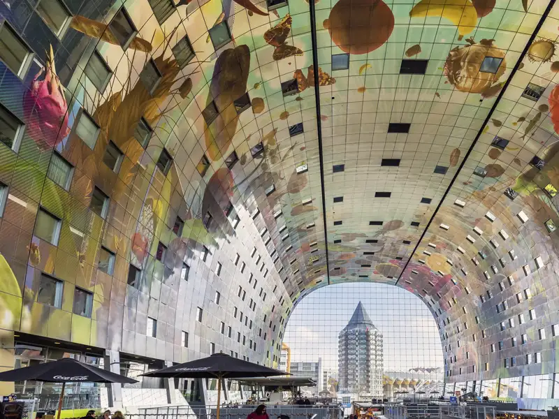 Besucher einer Studienreise unter der riesigen, gewölbten Decke der Markthalle in Rotterdam mit ihrem bunten Kunstwerk.