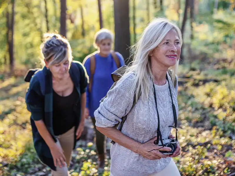 Drei Teilnehmerinnen einer Studienreise wandern auf den Spuren Fontanes gut gelaunt durch einen sonnigen Wald in Brandenburg, eine Tour auf unserer Eventreise mit Studiosus.