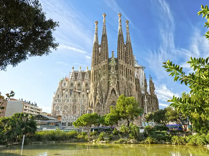 Bestaunen Sie Gaudís unvollendete Basilika Sagrada Família auf Ihrer Gruppenreise nach Barcelona, gesehen von einem Park mit einem See im Vordergrund bei Sonnenschein.