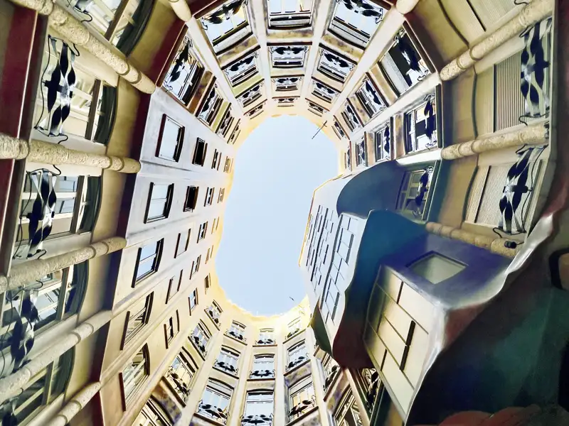 Auf einer Studienreise in Barcelona: Blick nach oben durch den geschwungenen Innenhof von Gaudís Casa Milà zum Himmel.