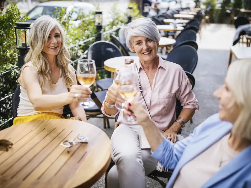 Drei Frauen einer Studiosus-Studienreise stoßen gut gelaunt in einem Straßencafé in Barcelona mit Wein an.