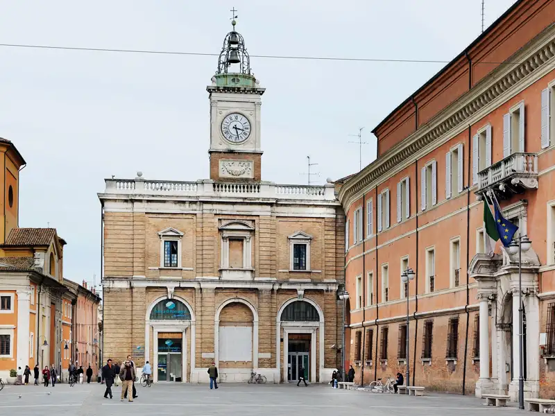 Auf unserer Gruppenreise entdecken wir die weitläufige Piazza del Popolo in Ravenna mit dem historischen Uhrturm des Palazzo Comunale und flanierenden Menschen.