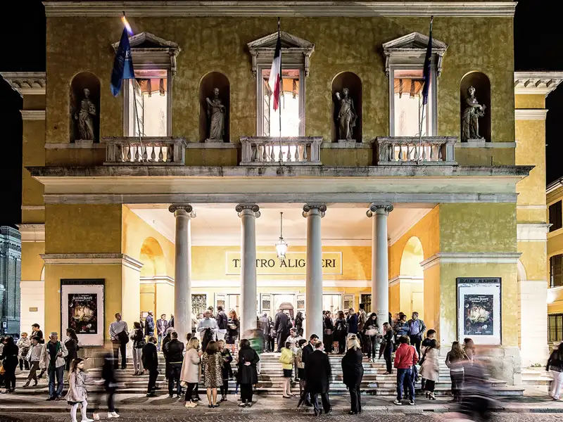 Elegant gekleidete Gäste einer Eventreise versammeln sich vor dem beleuchteten Teatro Alighieri in Ravenna.