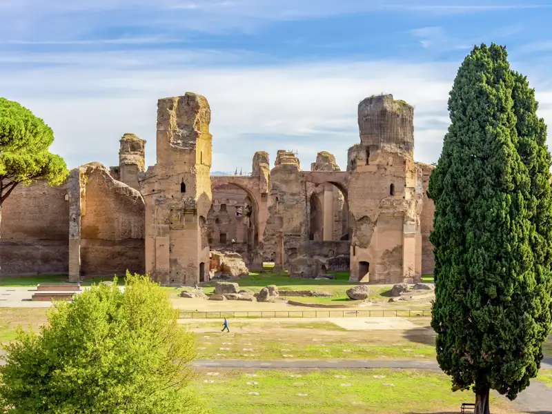 Bestaunen Sie die majestätische Ruinen der Caracalla-Thermen auf Ihrer Gruppenreise durch Rom, umgeben von einer weitläufigen Parkanlage mit Zypressen an einem sonnigen Tag.