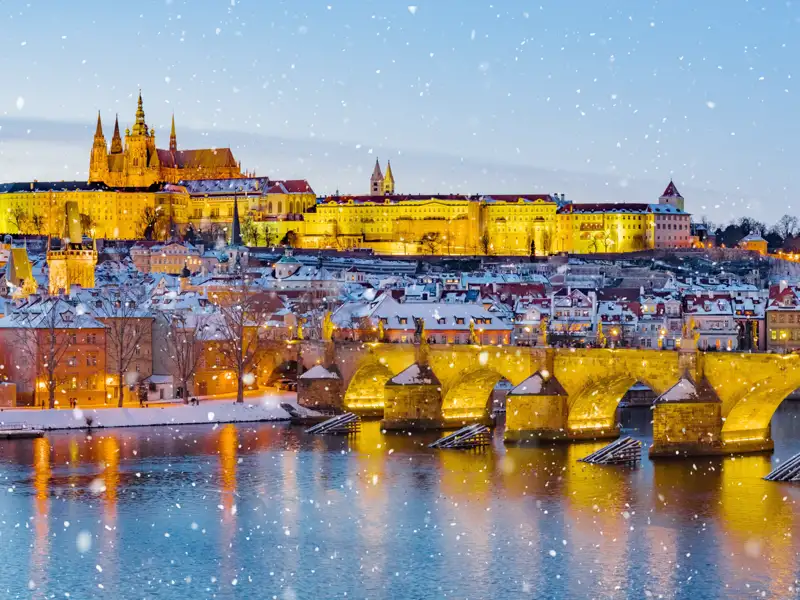 Die verschneite Karlsbrücke und die Prager Burg über der Moldau im abendlichen Lichterglanz bei Schneefall, sehen Sie auf Ihrer Eventreise mit Studiosus.