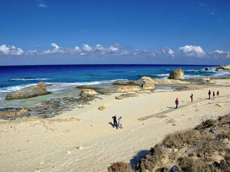 Kleine Gruppe einer Studiosus Studienreise am Kleopatra-Strand bei Marsa Matruh mit Felsen im türkisfarbenen Mittelmeer.