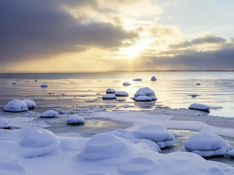 Stimmungsvoller Sonnenuntergang über der vereisten Ostseeküste Estlands mit schneebedeckten Steinen am Ufer, auch für unsere Studiosus Reisegruppe zu entdecken.