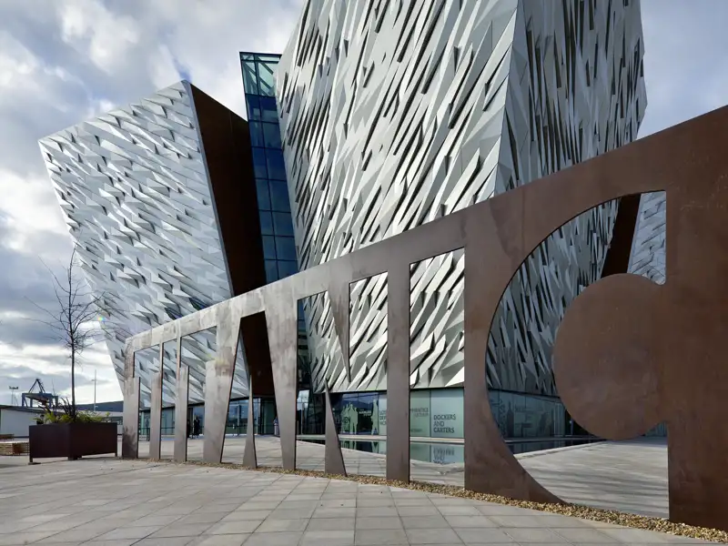 Der markante TITANIC-Schriftzug vor der modernen, an einen Schiffsbug erinnernden Fassade des Museums in Belfast.