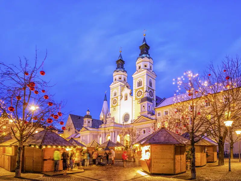 Stimmungsvoller Weihnachtsmarkt in Brixen mit beleuchteten Holzhütten vor der Kulisse des Doms in der Abenddämmerung, zu erleben auf ihrer Studiosus Silvesterreise.
