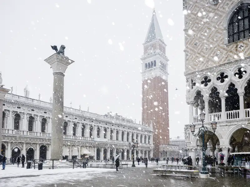 Blick auf den verschneiten Markusplatz mit vielen vereinzelten Menschen, die die Schönheit der Stadt im Winter einfangen. Auch für Sie auf unserer Studiosus Eventreise zu entdecken - vieelicht mit Schnee.